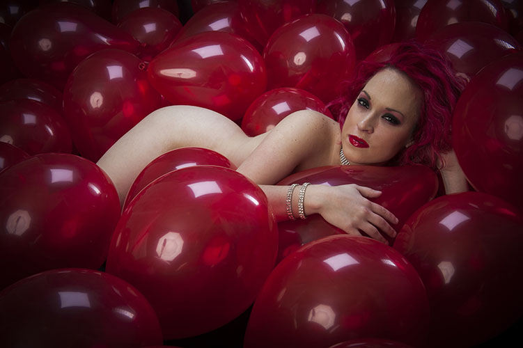 Implied nude female model laying in red balloons in photo studio in Nashville
