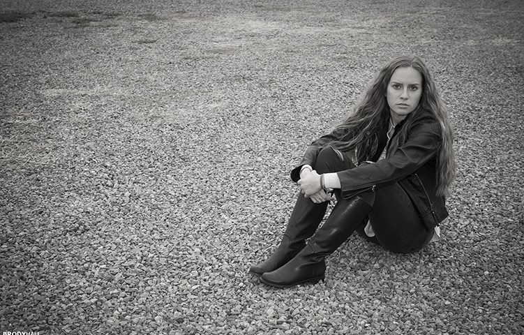 Young adult female model sitting on gravel parking lot in Colorado