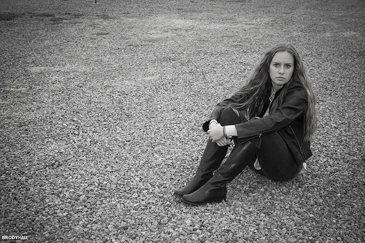 Young adult female model sitting on gravel parking lot in Colorado
