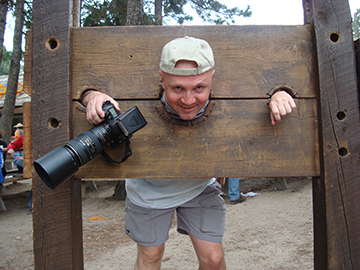 Brody in wooden stocks holding camera at the renn fair in Larkspur, CO
